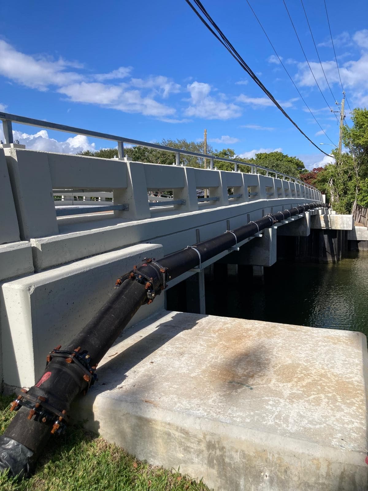 A recently completed replacement bridge with tall concrete barriers, metal railing and a large utility pipe bolted along its side